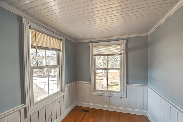 unfurnished room with wood finished floors, wood ceiling, visible vents, wainscoting, and crown molding