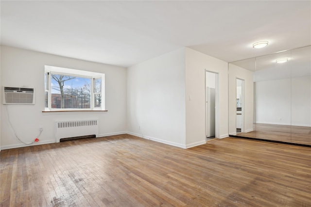 empty room with radiator, a wall mounted air conditioner, and light wood-type flooring