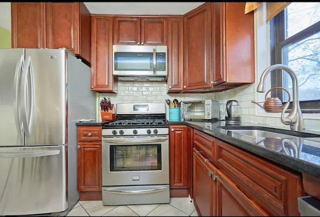 kitchen featuring light tile patterned floors, sink, stainless steel appliances, and dark stone countertops