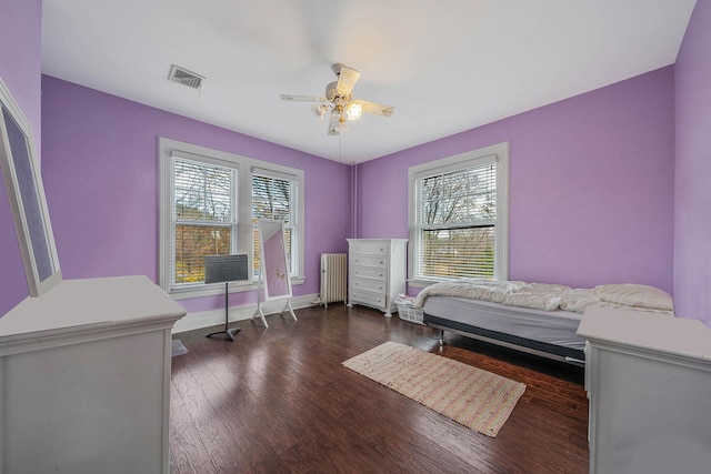 bedroom with ceiling fan, dark wood-type flooring, radiator, and multiple windows