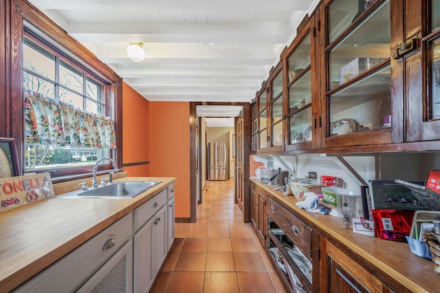 kitchen featuring beam ceiling, light tile patterned floors, stainless steel refrigerator, and sink