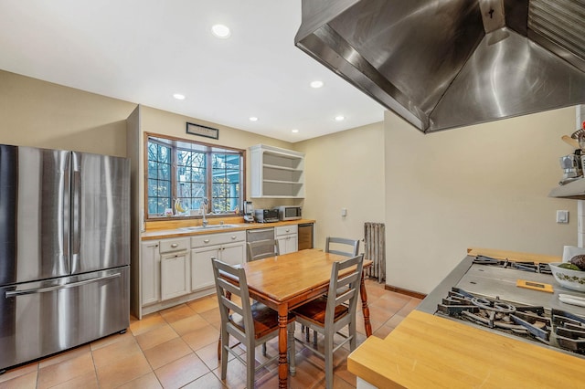 kitchen with sink, light tile patterned floors, appliances with stainless steel finishes, island range hood, and white cabinetry