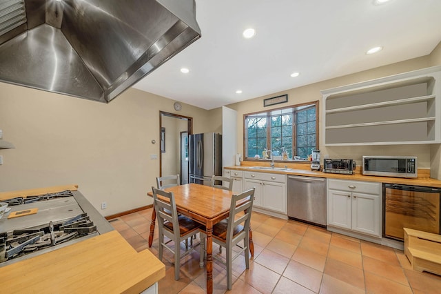 kitchen featuring wood counters, appliances with stainless steel finishes, sink, white cabinetry, and range hood