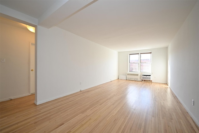 unfurnished room with beamed ceiling, radiator heating unit, and light hardwood / wood-style flooring