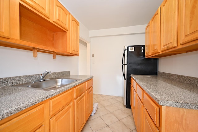 kitchen with light tile patterned flooring, black fridge, and sink