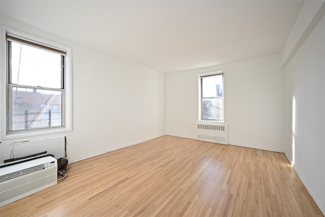 spare room with radiator heating unit, light hardwood / wood-style floors, and a wall mounted AC