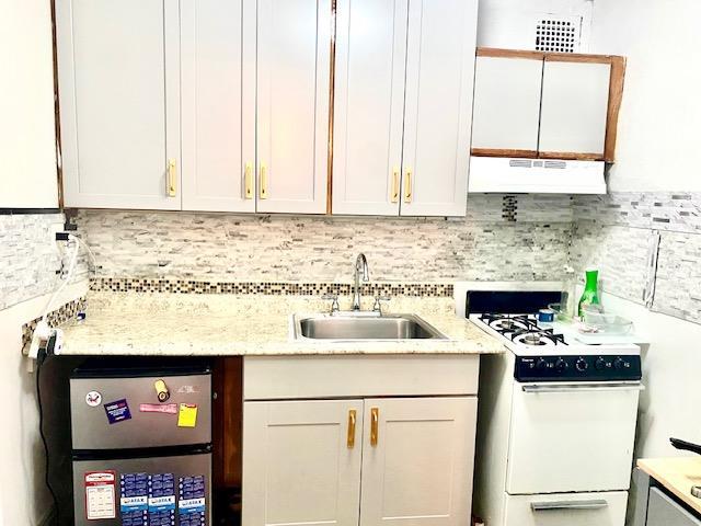 kitchen featuring tasteful backsplash, extractor fan, sink, white cabinets, and white stove