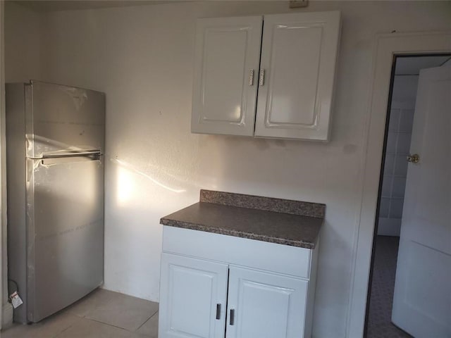 kitchen with stainless steel fridge, light tile patterned floors, electric panel, and white cabinetry