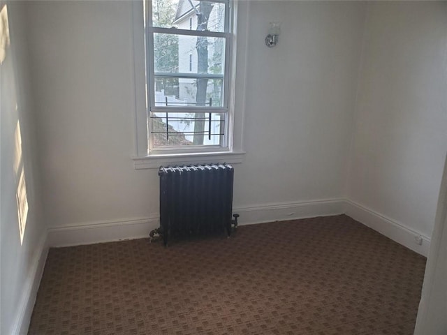 unfurnished room featuring radiator heating unit and dark carpet