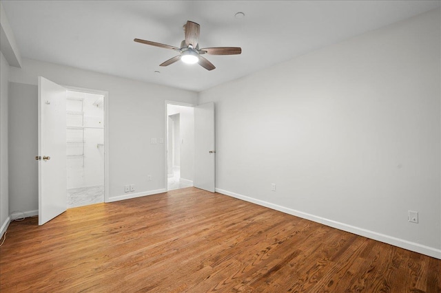 unfurnished bedroom featuring ceiling fan, a closet, a walk in closet, and light wood-type flooring