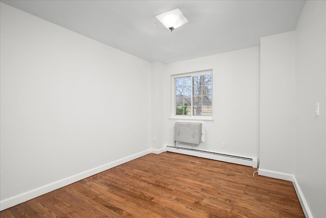 empty room featuring baseboard heating and hardwood / wood-style floors