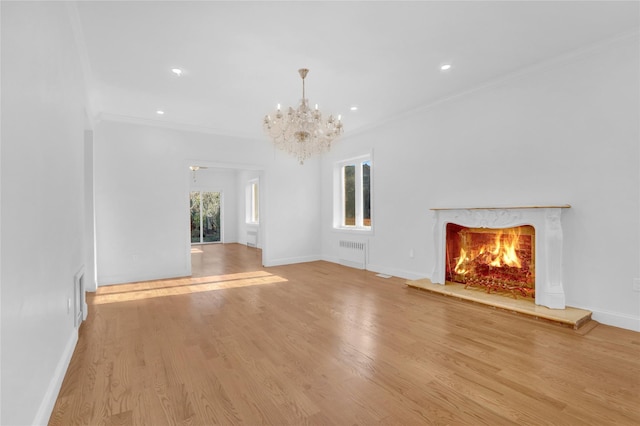 unfurnished living room featuring radiator, an inviting chandelier, crown molding, light wood-type flooring, and a premium fireplace