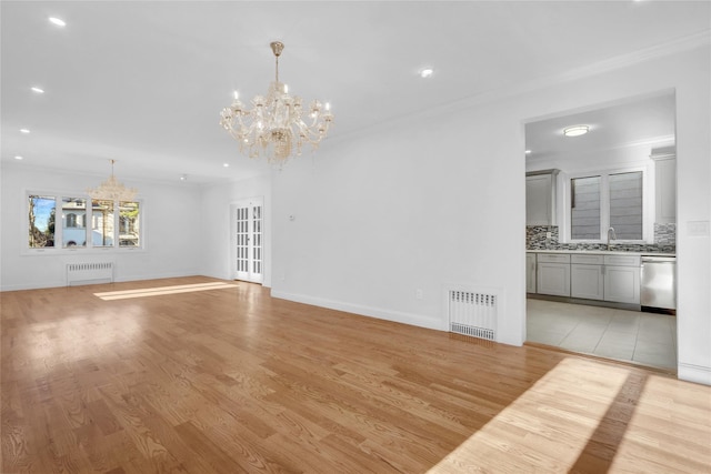 unfurnished living room with a chandelier, light hardwood / wood-style flooring, radiator, and sink