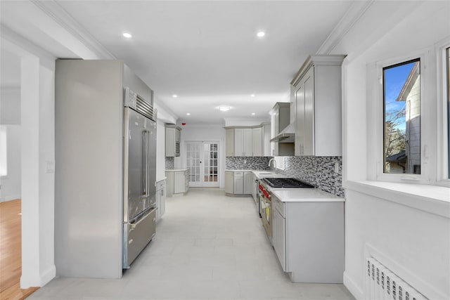 kitchen with gray cabinetry, backsplash, radiator, built in fridge, and crown molding