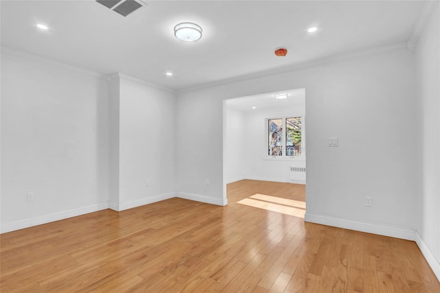 empty room with light wood-type flooring, crown molding, and radiator