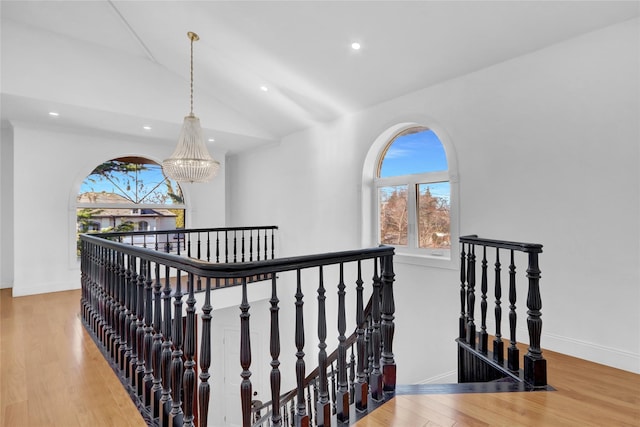 hall with hardwood / wood-style floors, vaulted ceiling, and a chandelier