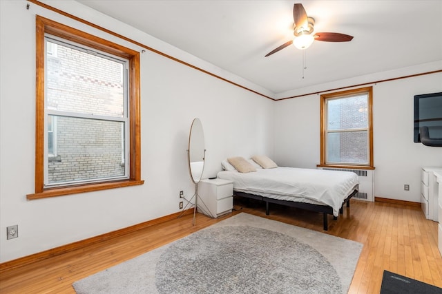 bedroom featuring multiple windows, ceiling fan, radiator heating unit, and light hardwood / wood-style flooring