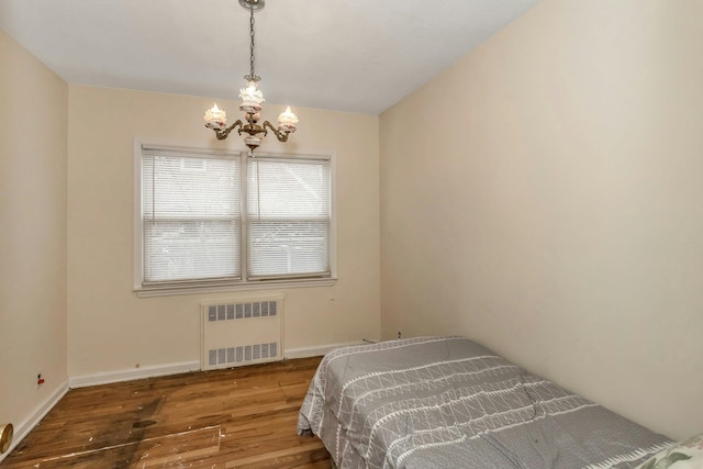 bedroom featuring radiator, wood-type flooring, and an inviting chandelier