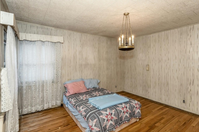 bedroom featuring a chandelier, wood-type flooring, and wooden walls