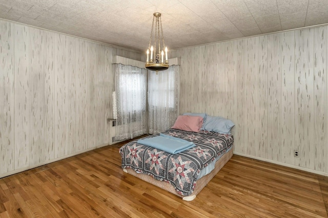 bedroom featuring wood-type flooring, an inviting chandelier, and wooden walls