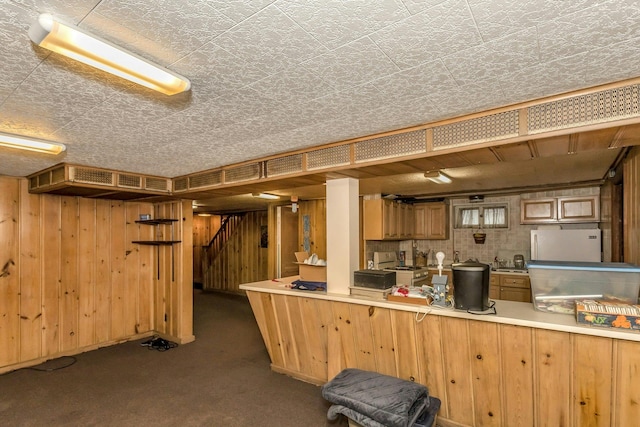 kitchen with carpet flooring, kitchen peninsula, wood walls, and white appliances