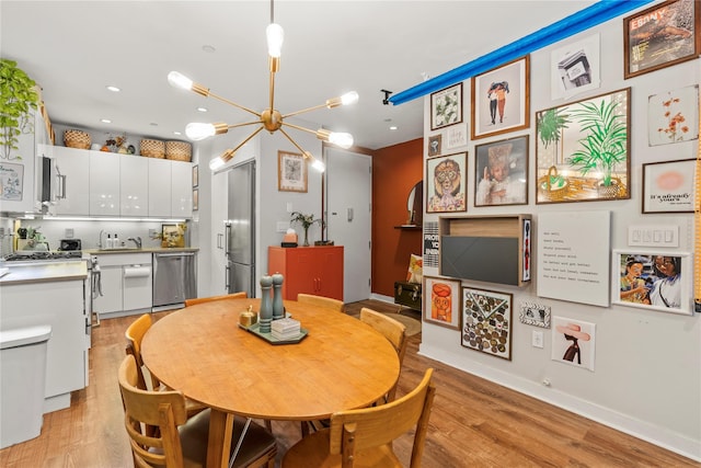 dining area with light hardwood / wood-style floors, an inviting chandelier, and sink