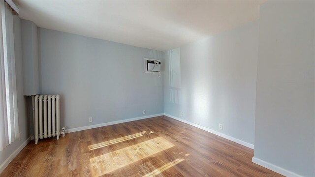 unfurnished room with wood-type flooring, radiator heating unit, and a wall unit AC