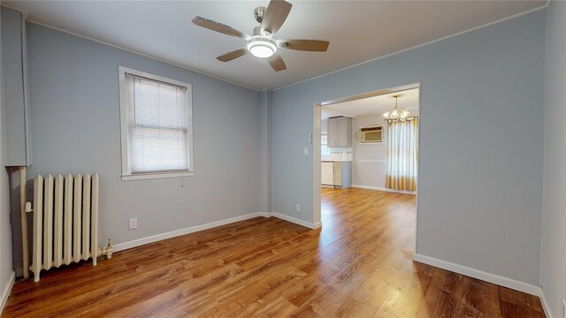 empty room featuring hardwood / wood-style floors, ceiling fan with notable chandelier, a wall unit AC, and radiator