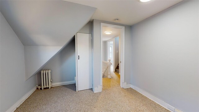 bonus room featuring light colored carpet, radiator, and vaulted ceiling