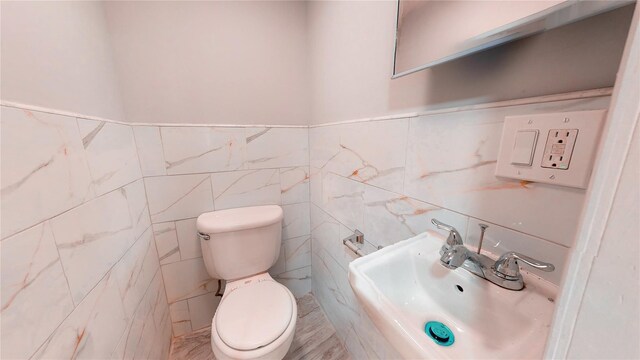 bathroom with toilet, sink, and tile walls