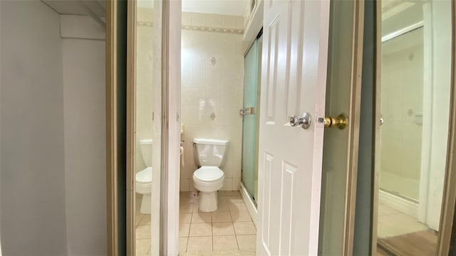 bathroom with tile patterned flooring, toilet, tile walls, and an enclosed shower