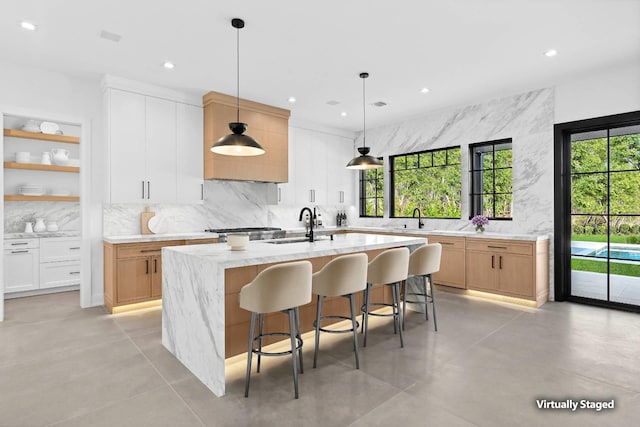 kitchen with sink, white cabinetry, tasteful backsplash, decorative light fixtures, and an island with sink