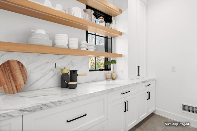 bar featuring light stone counters, dark tile patterned floors, decorative backsplash, and white cabinets