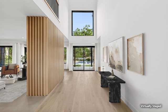 corridor with hardwood / wood-style floors, a healthy amount of sunlight, and a high ceiling