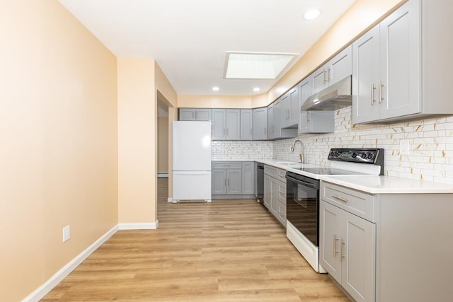 kitchen with gray cabinetry, white appliances, sink, a skylight, and light wood-type flooring