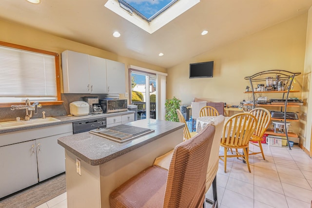 kitchen with vaulted ceiling with skylight, sink, dishwasher, a center island, and white cabinetry