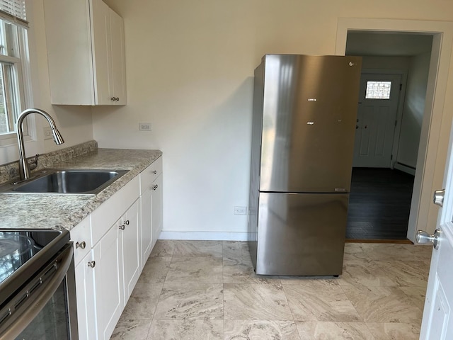 kitchen featuring light stone counters, stainless steel appliances, baseboard heating, sink, and white cabinetry