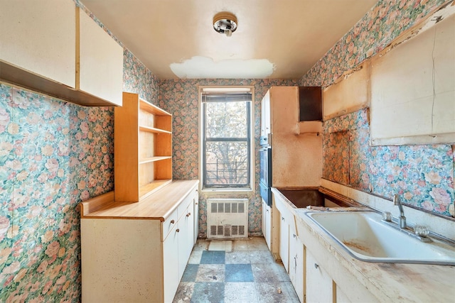 kitchen with sink, radiator heating unit, white cabinets, and stainless steel oven