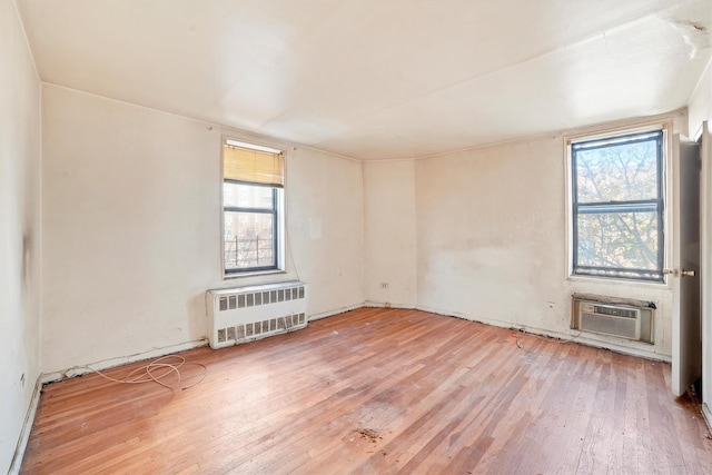 spare room featuring a wall mounted air conditioner, radiator heating unit, and wood-type flooring