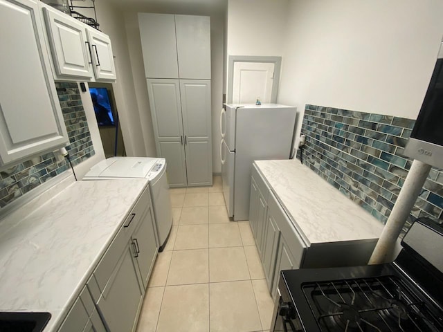 kitchen featuring light tile patterned flooring, backsplash, gray cabinets, separate washer and dryer, and white fridge