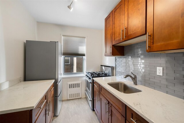 kitchen with decorative backsplash, appliances with stainless steel finishes, brown cabinetry, a sink, and light stone countertops