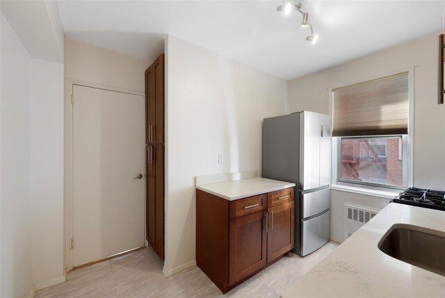 kitchen featuring light countertops, radiator heating unit, freestanding refrigerator, a sink, and baseboards