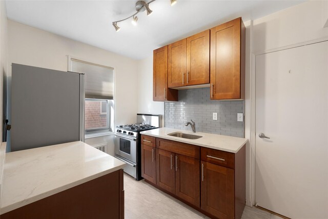 kitchen with brown cabinets, tasteful backsplash, appliances with stainless steel finishes, a sink, and light stone countertops