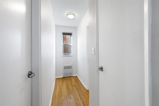 hall with light wood-style floors, radiator heating unit, and baseboards