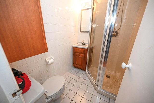 bathroom with tile patterned flooring, toilet, a shower with door, vanity, and tile walls