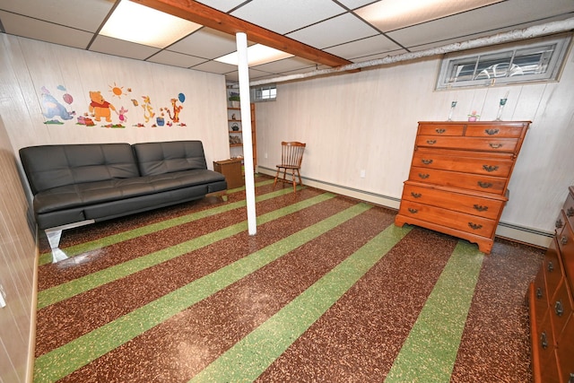 basement with a paneled ceiling, wooden walls, and a baseboard heating unit