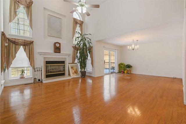 unfurnished living room with ceiling fan with notable chandelier, a high ceiling, and light hardwood / wood-style flooring