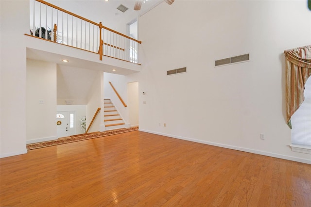 unfurnished living room with ceiling fan, wood-type flooring, and a high ceiling