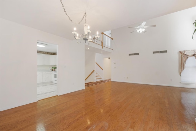 unfurnished living room with a towering ceiling, ceiling fan with notable chandelier, and light wood-type flooring