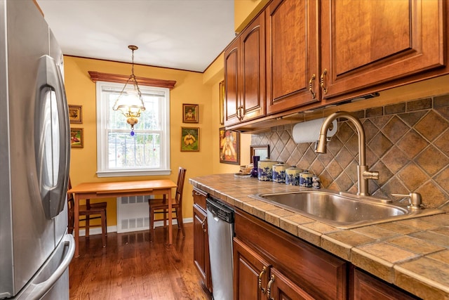 kitchen featuring decorative light fixtures, dark wood-type flooring, stainless steel appliances, tasteful backsplash, and sink